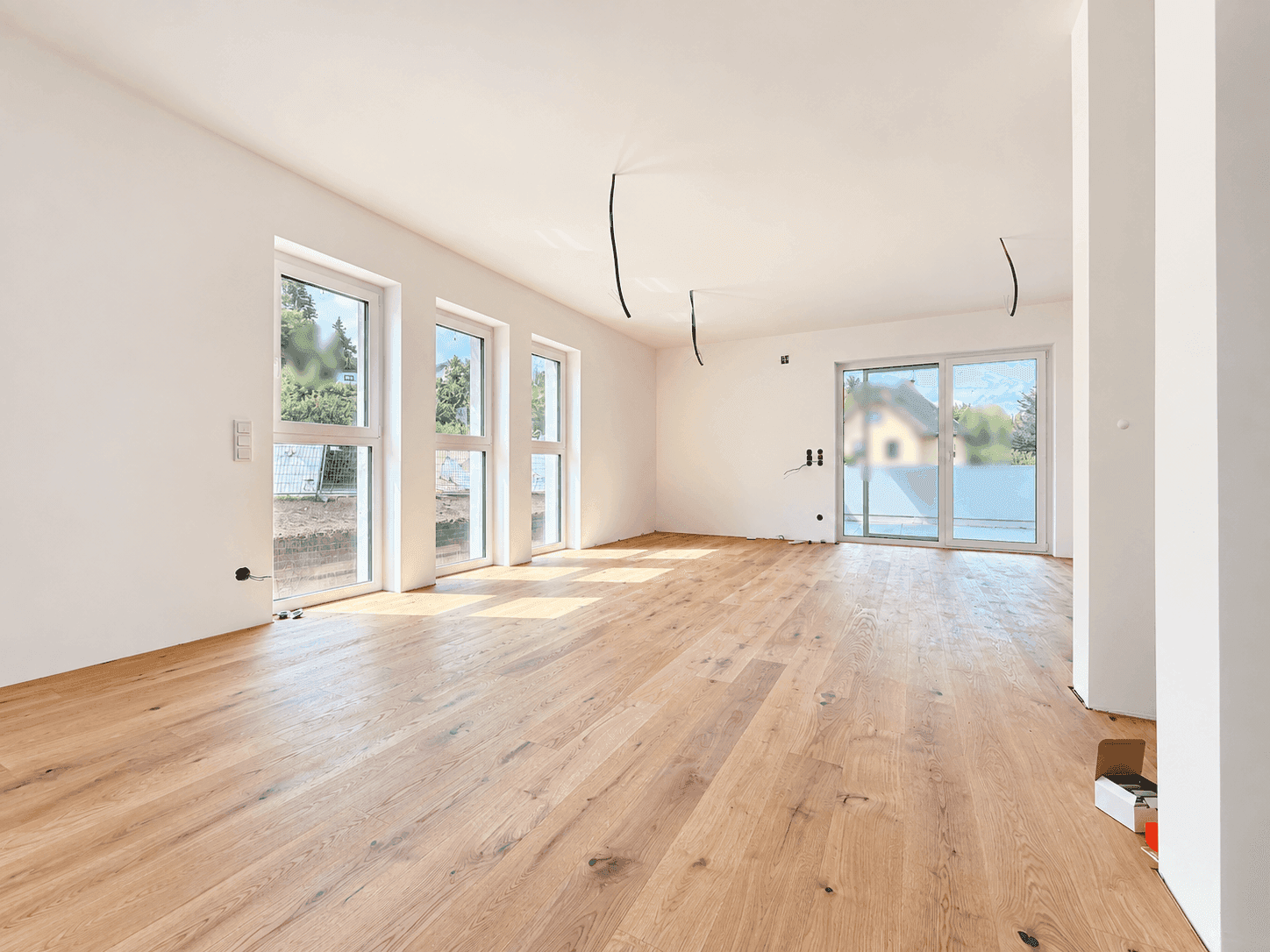 Heller, leerer Raum mit neuem Holzboden und großen Fenstern, bereit für den Innenausbau.