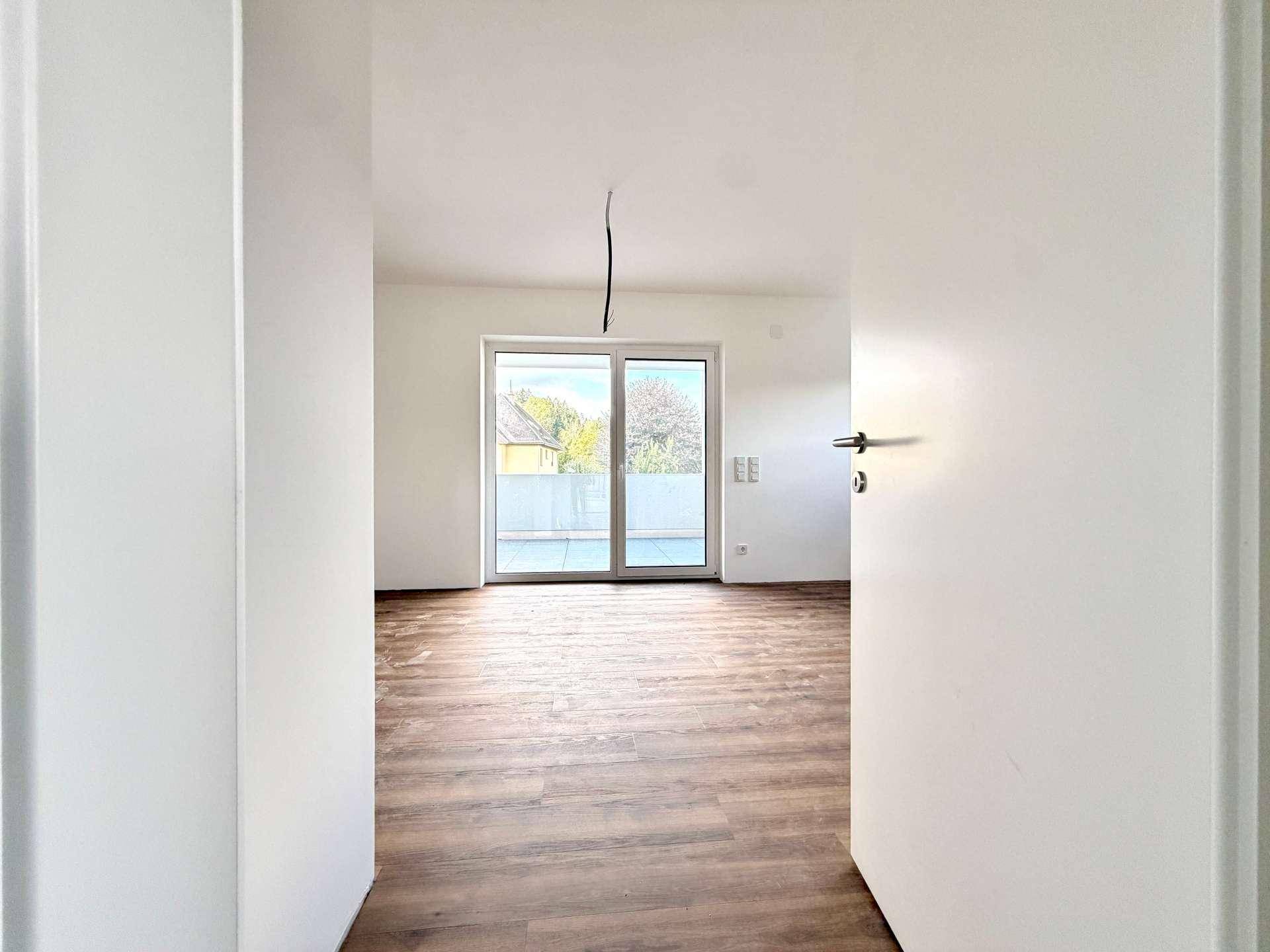 Heller, leerer Raum mit Laminatboden und Zugang zu einem Außenbereich durch eine große Schiebetür.