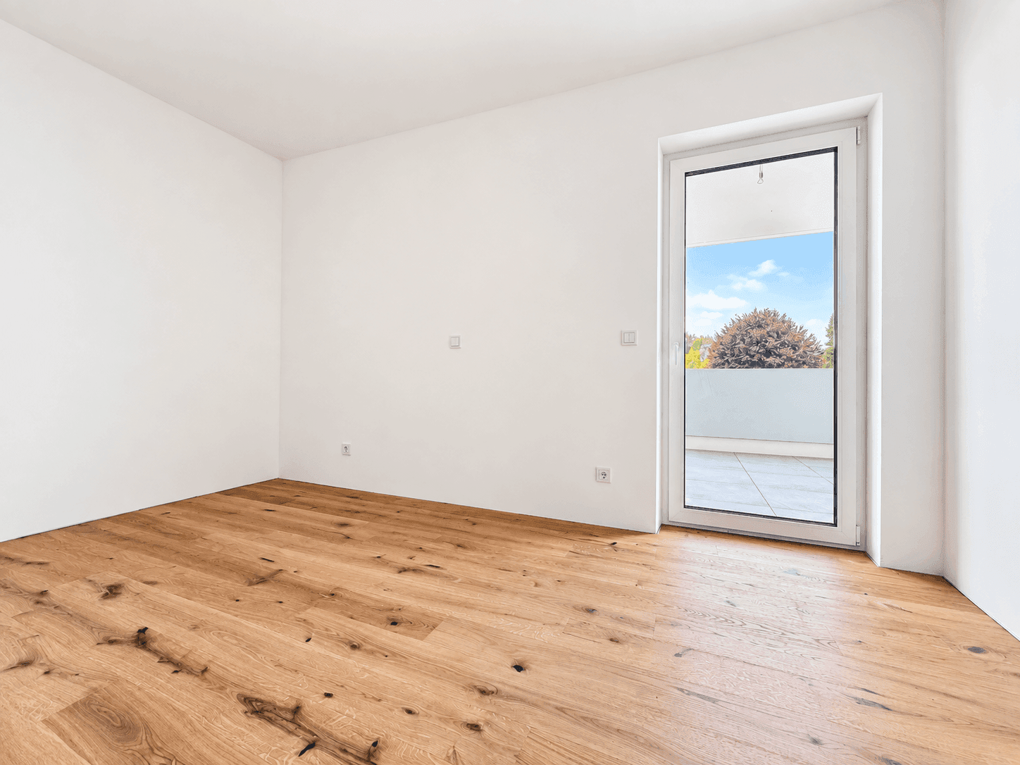 Heller Raum mit Holzboden und Zugang zu einem Außenbereich, ideal für ein Schlafzimmer.