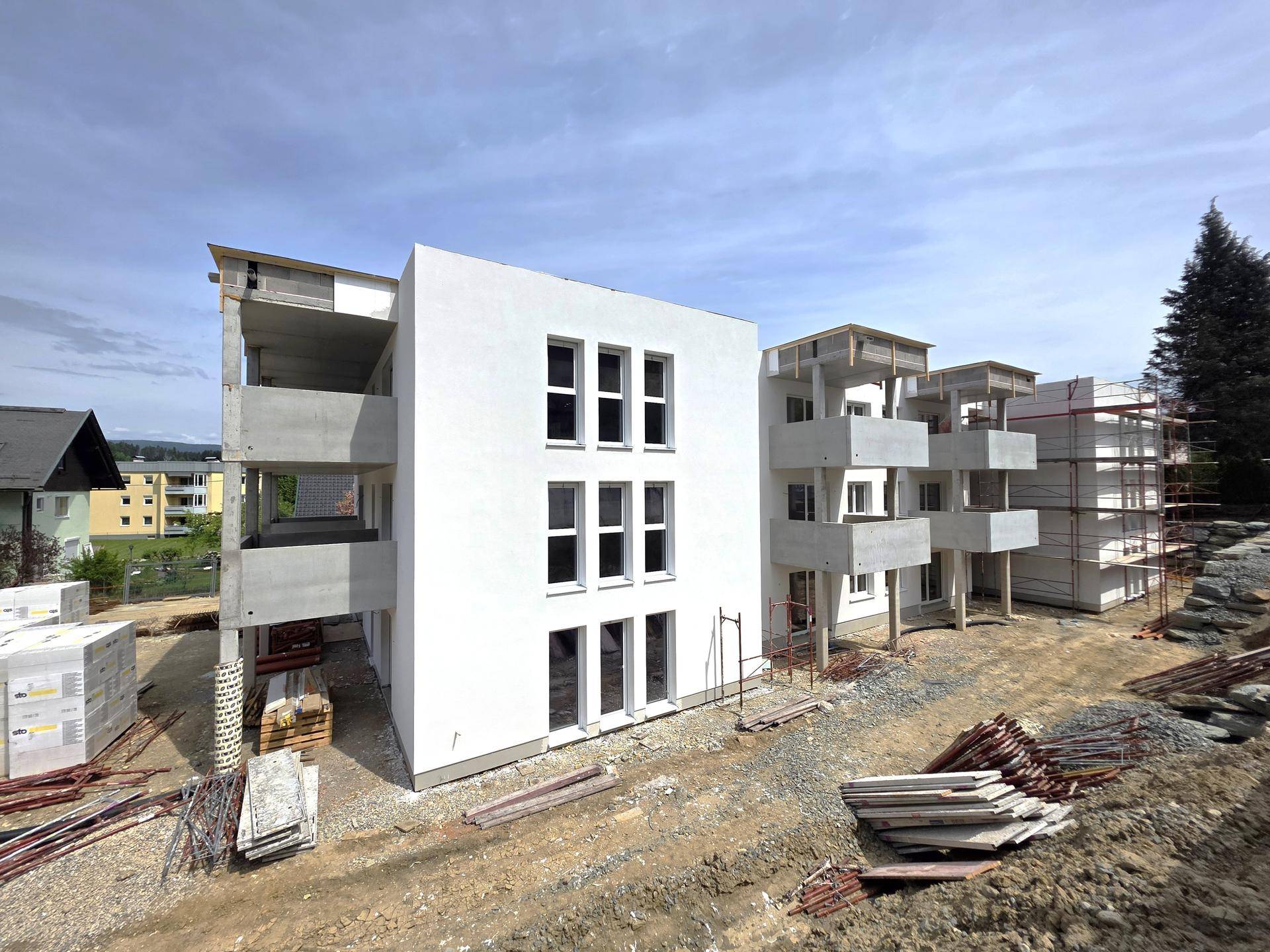 Neubau-Wohngebäude in Bauphase mit bereits verputzter Fassade und sichtbaren Balkonen.