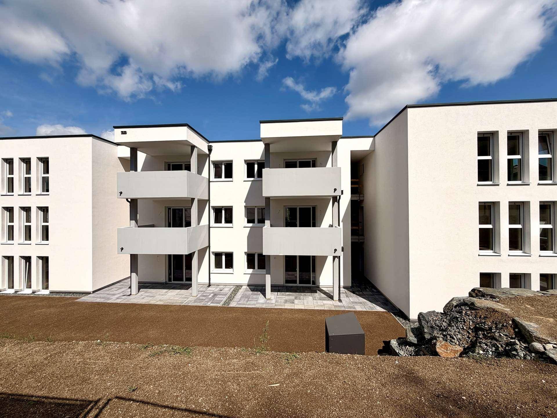 Moderne Wohnanlage mit weißer Fassade und grauen Balkonen, umgeben von Baustellenbereich.