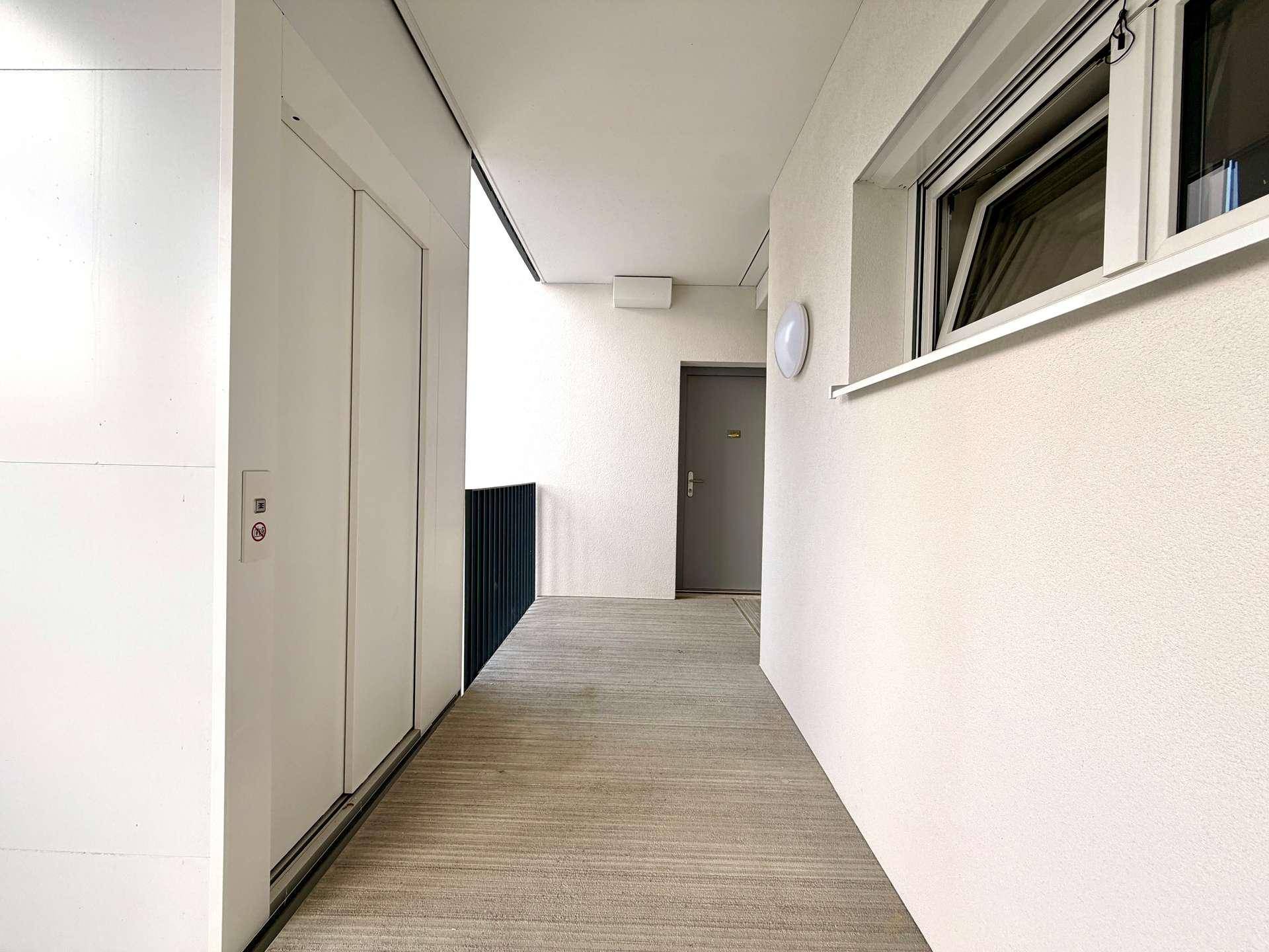 Heller Flur im Gebäude mit Zugang zu einem modernen Aufzug und weiteren Wohneinheiten.