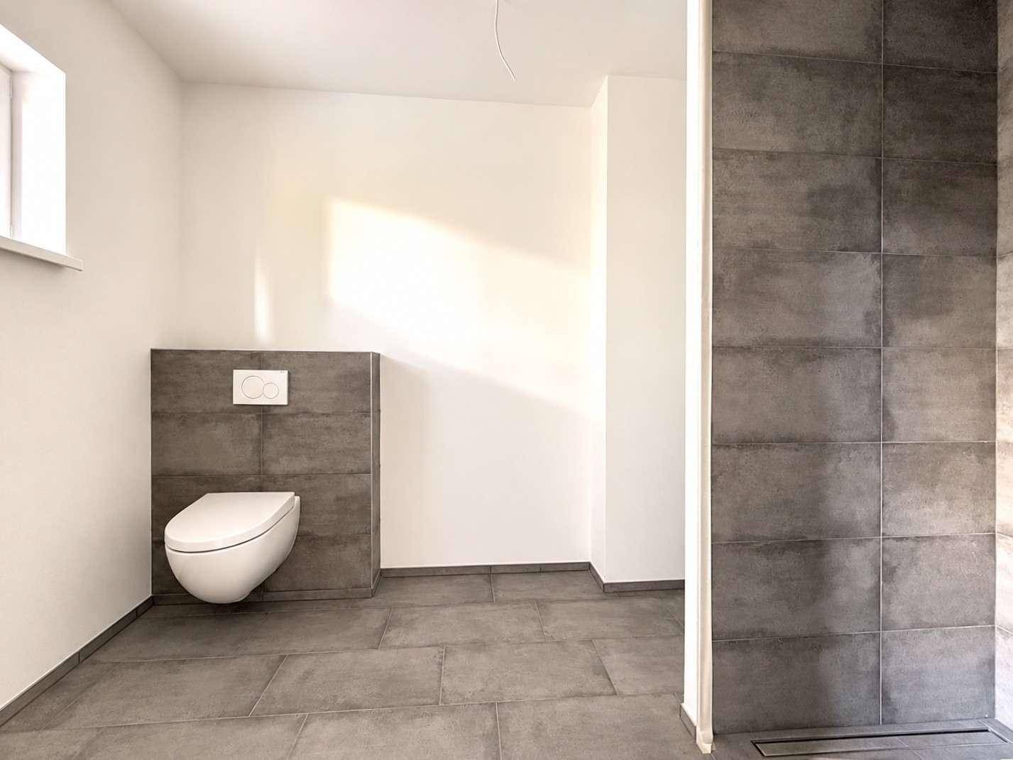 Modernes Badezimmer mit wandhängendem WC und großformatigen grauen Fliesen.