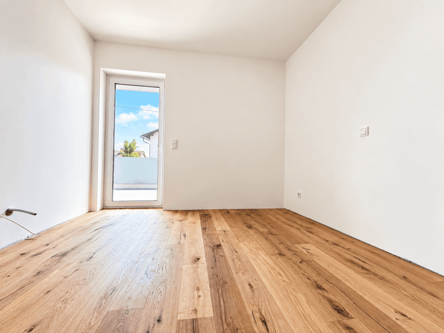 Leeres Zimmer mit Holzboden und Zugang zu einem Außenbereich, perfekt für ein Gästezimmer.