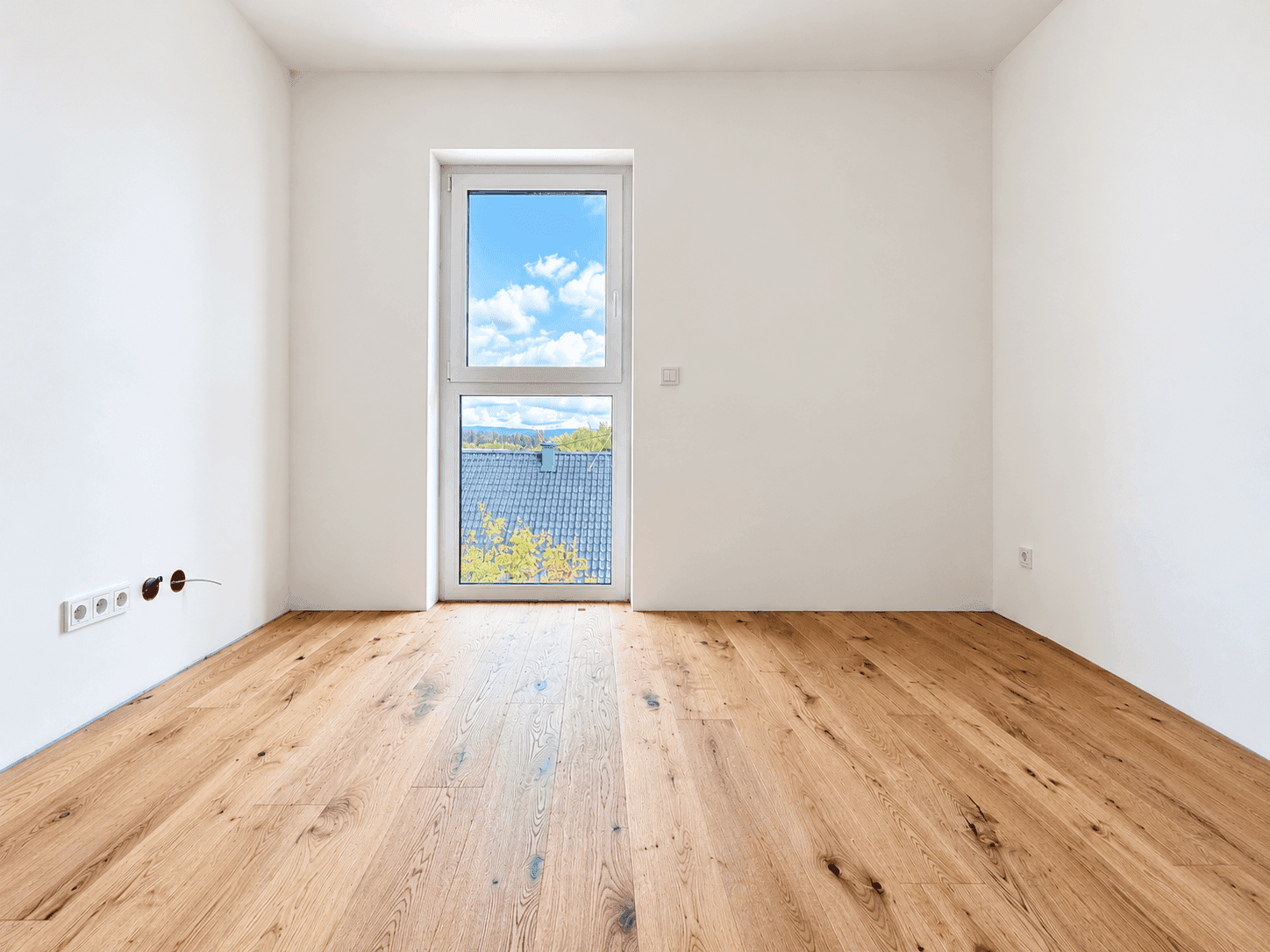 Helles Zimmer mit Holzboden und einem Fenster, das einen Blick auf die Umgebung bietet.