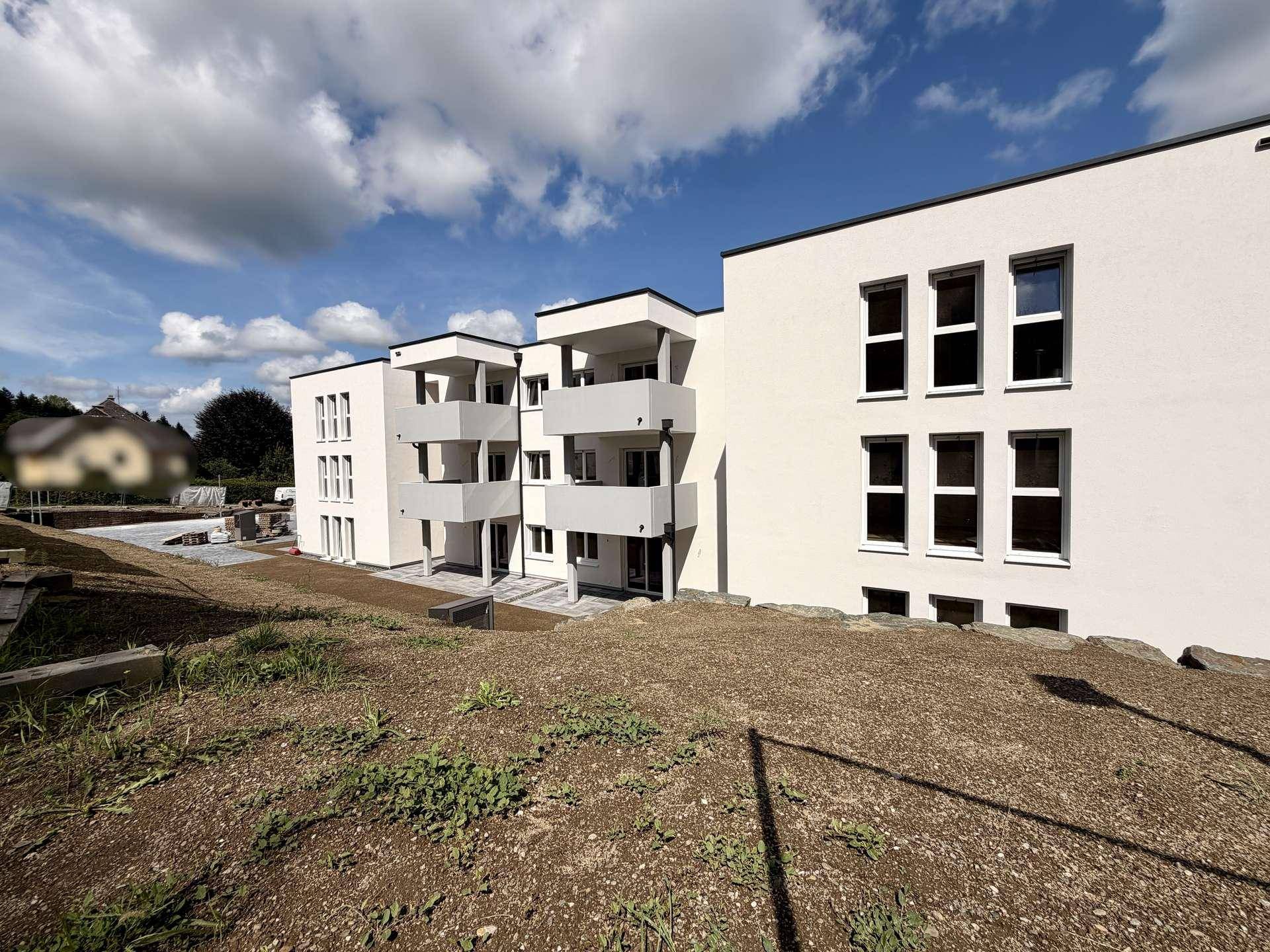 Neubau-Mehrfamilienhaus mit moderner Architektur und Balkonen in ländlicher Umgebung.