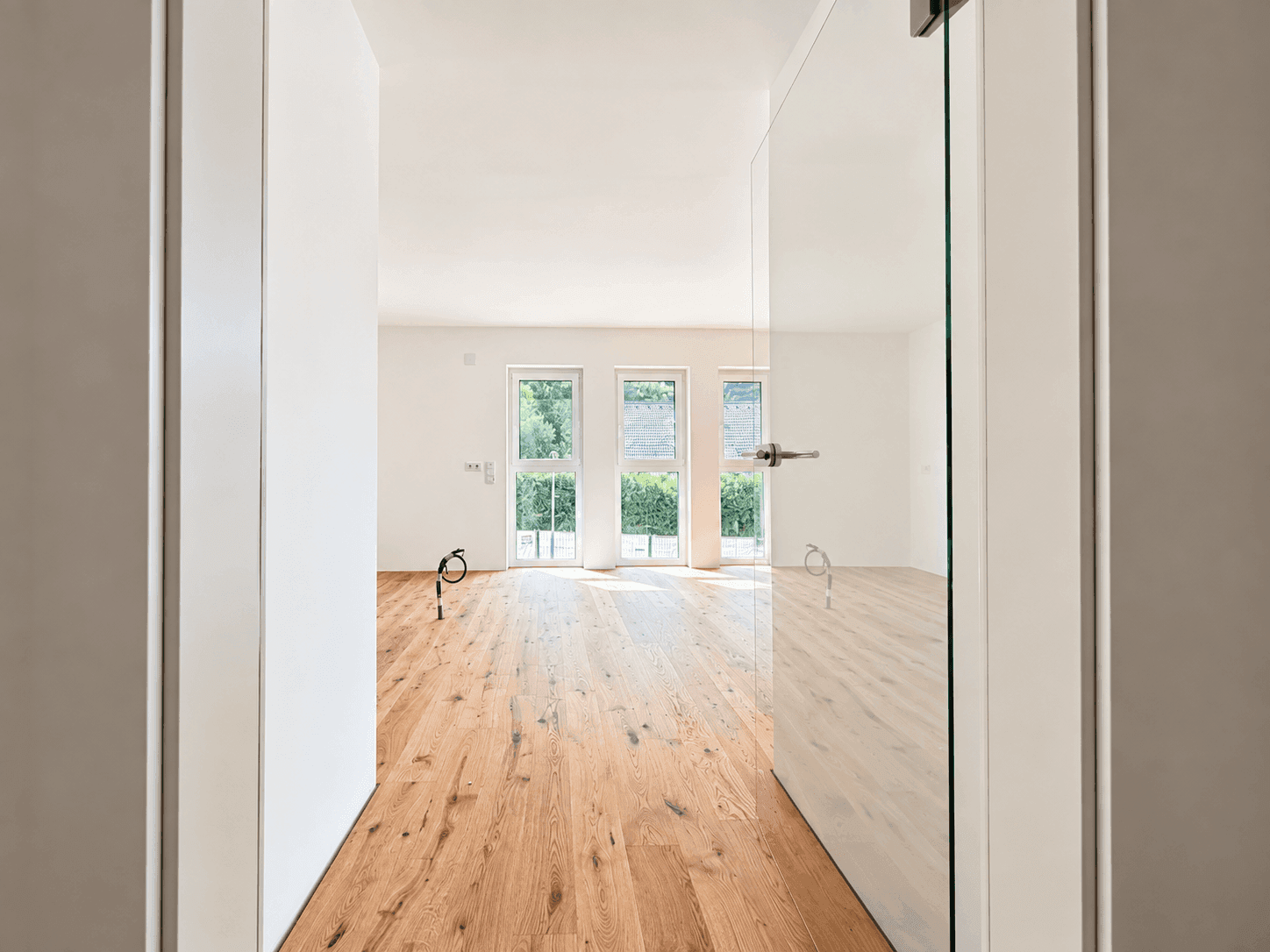 Heller, leerer Raum mit Holzboden und großen Fenstern, bereit für die Einrichtung.