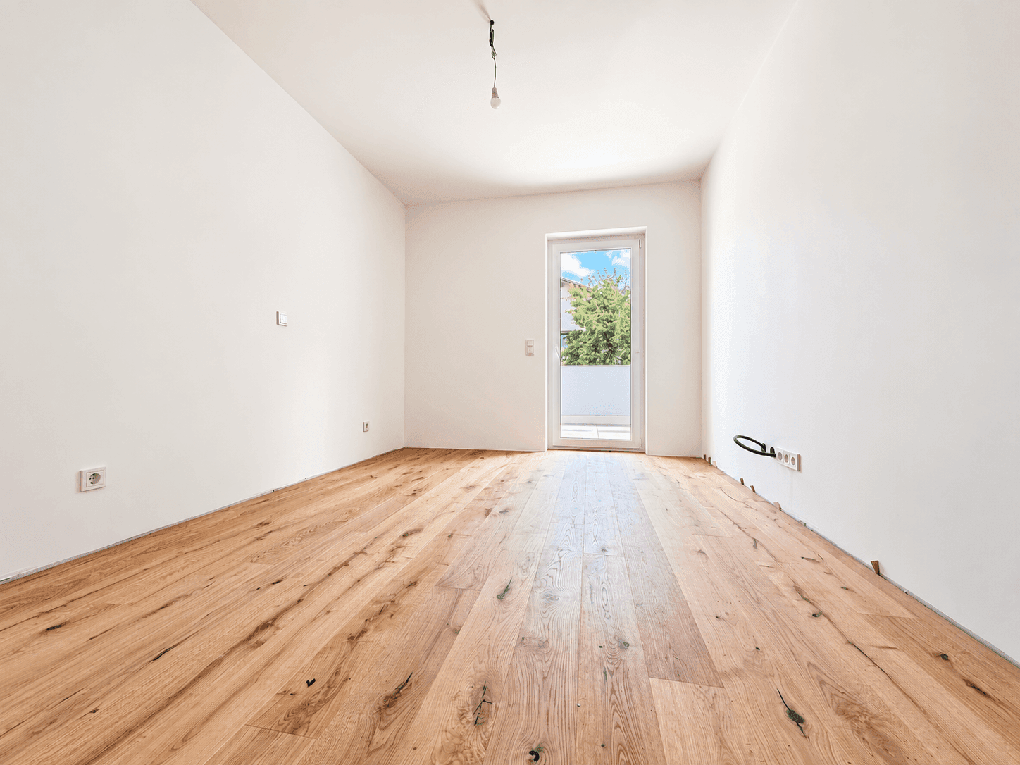 Leeres Zimmer mit Holzboden und Zugang zu einem Balkon, ideal als Schlaf- oder Arbeitszimmer.