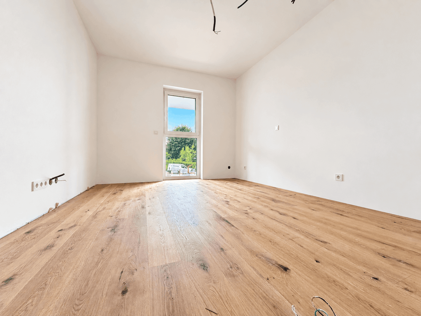 Leeres Zimmer mit Holzboden und Zugang zu einem Außenbereich, ideal als Schlaf- oder Arbeitszimmer.