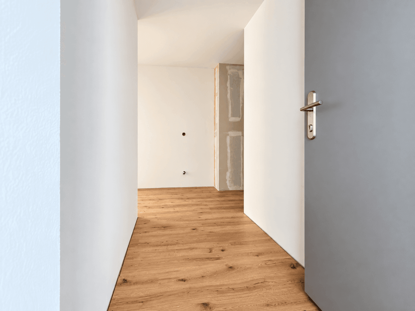 Heller Flur mit Holzboden und weiß gestrichenen Wänden, der zu weiteren Räumen führt.