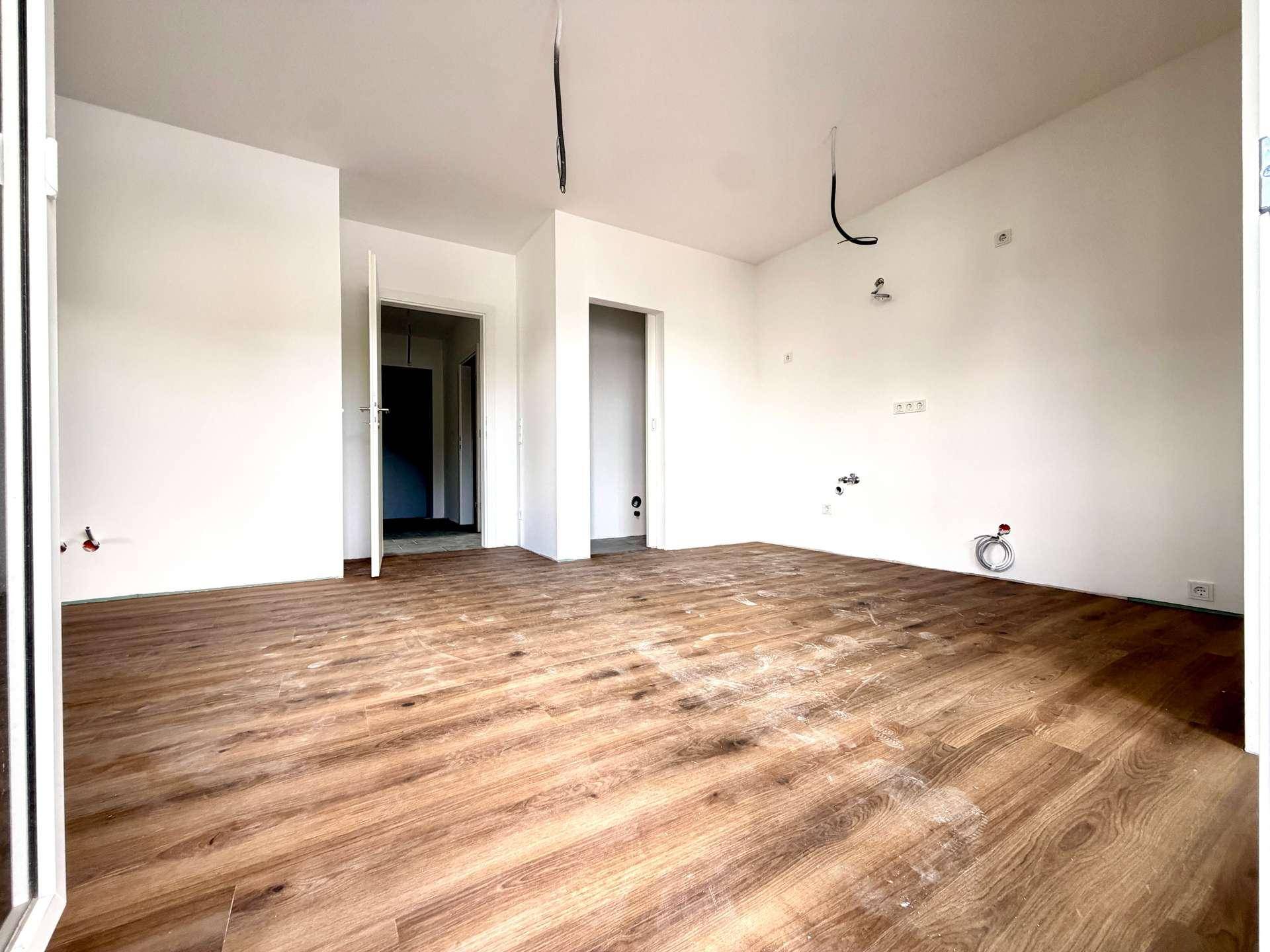 Leerer Raum mit Laminatboden und weißen Wänden, bereit für die weitere Gestaltung.