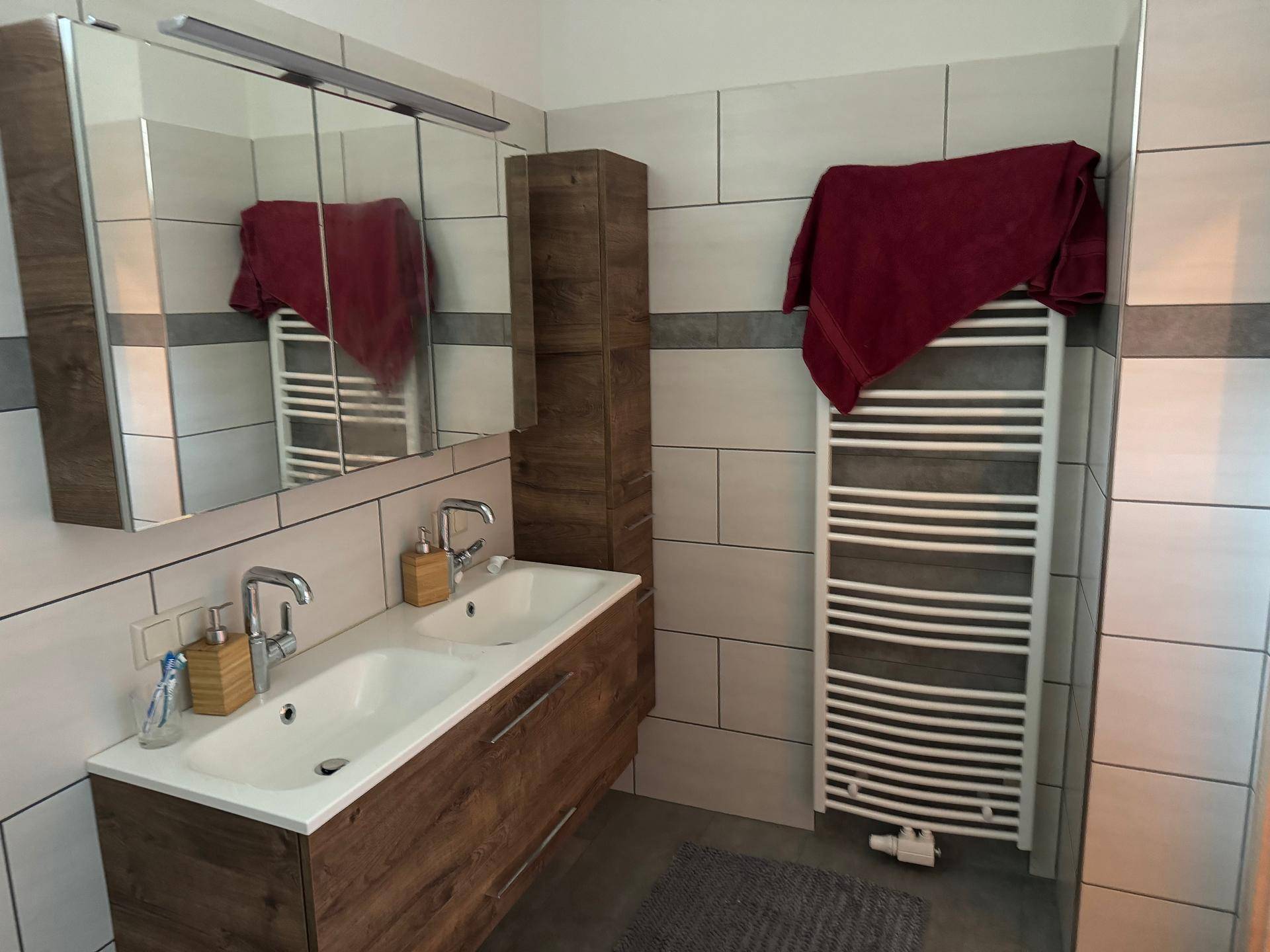 Badezimmer mit Doppelwaschbecken, Spiegelschrank und beheiztem Handtuchhalter.