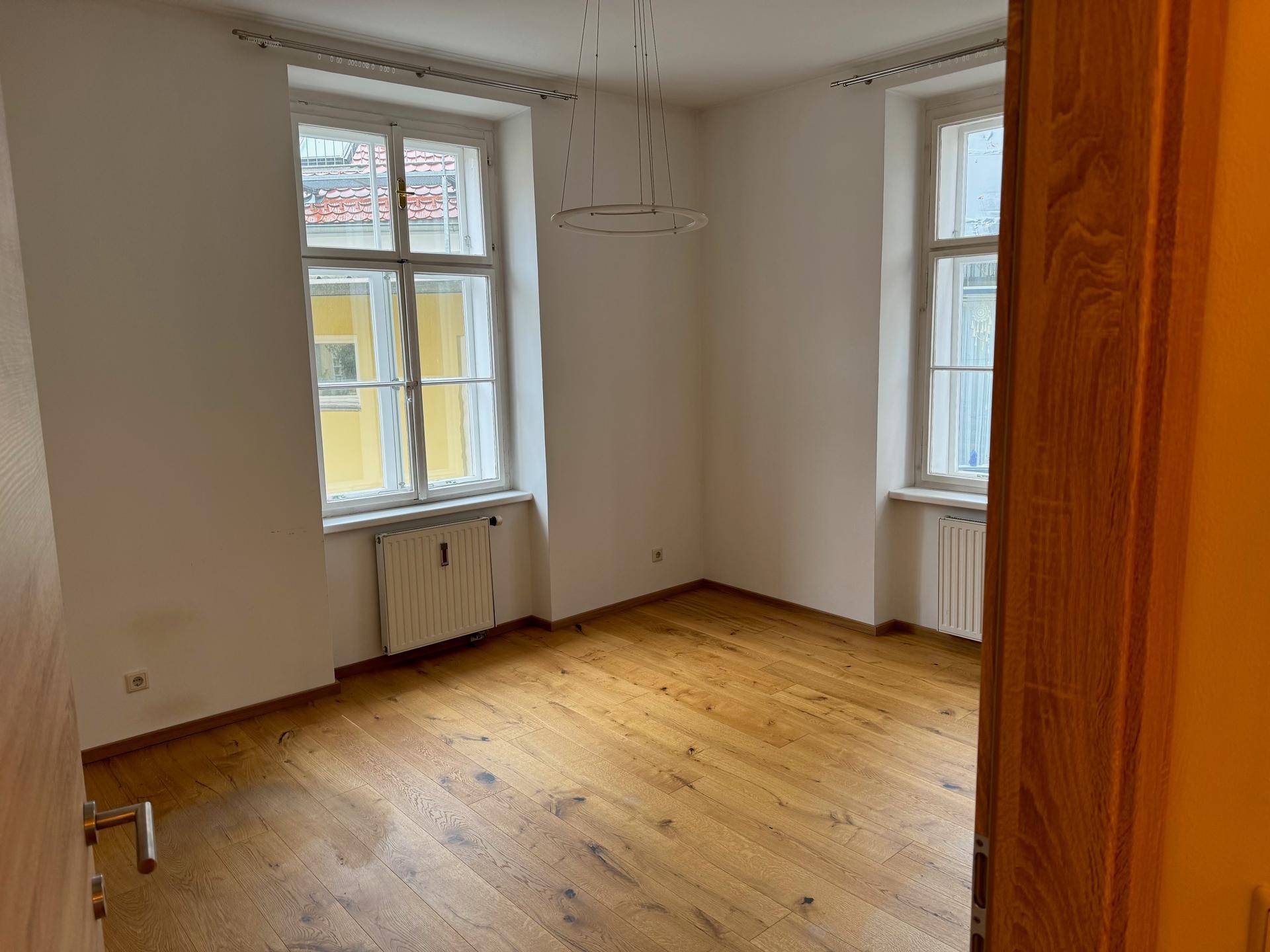 Geräumiger, heller Raum mit zwei Fenstern und Holzdielenboden.