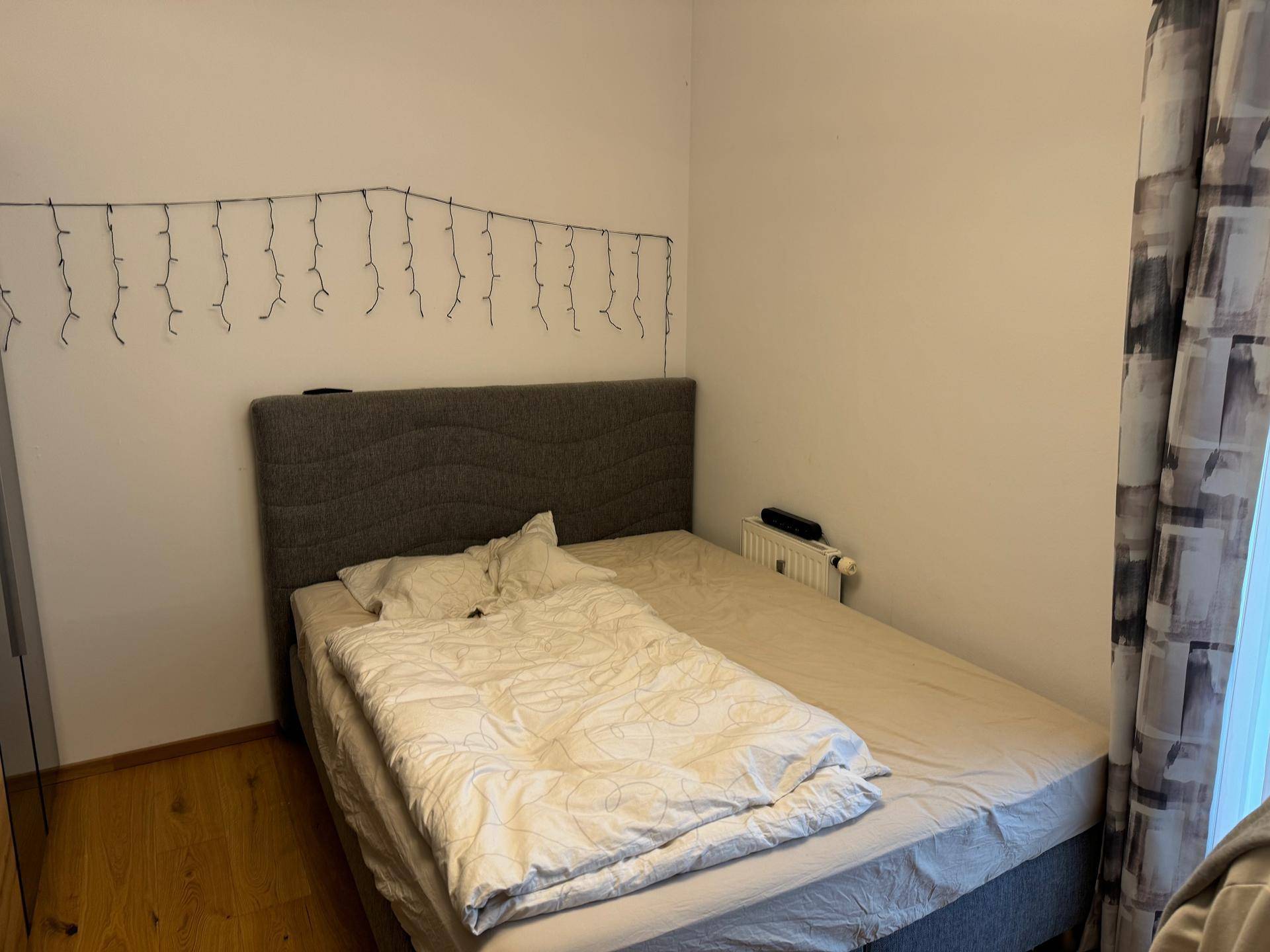 Schlafzimmer mit Bett, Holzboden und Fenster mit Vorhang.