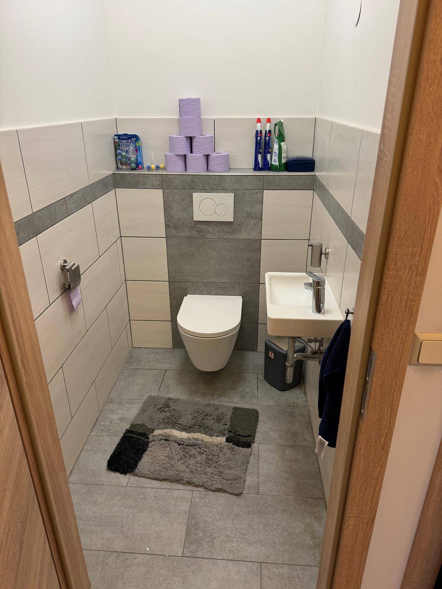 Modern gefliestes Gäste-WC mit wandhängender Toilette und kleinem Waschbecken.