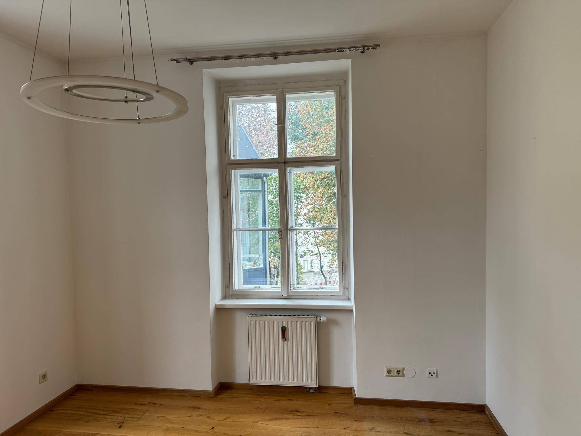 Heller Raum mit Holzboden, großem Fenster und Heizkörper.