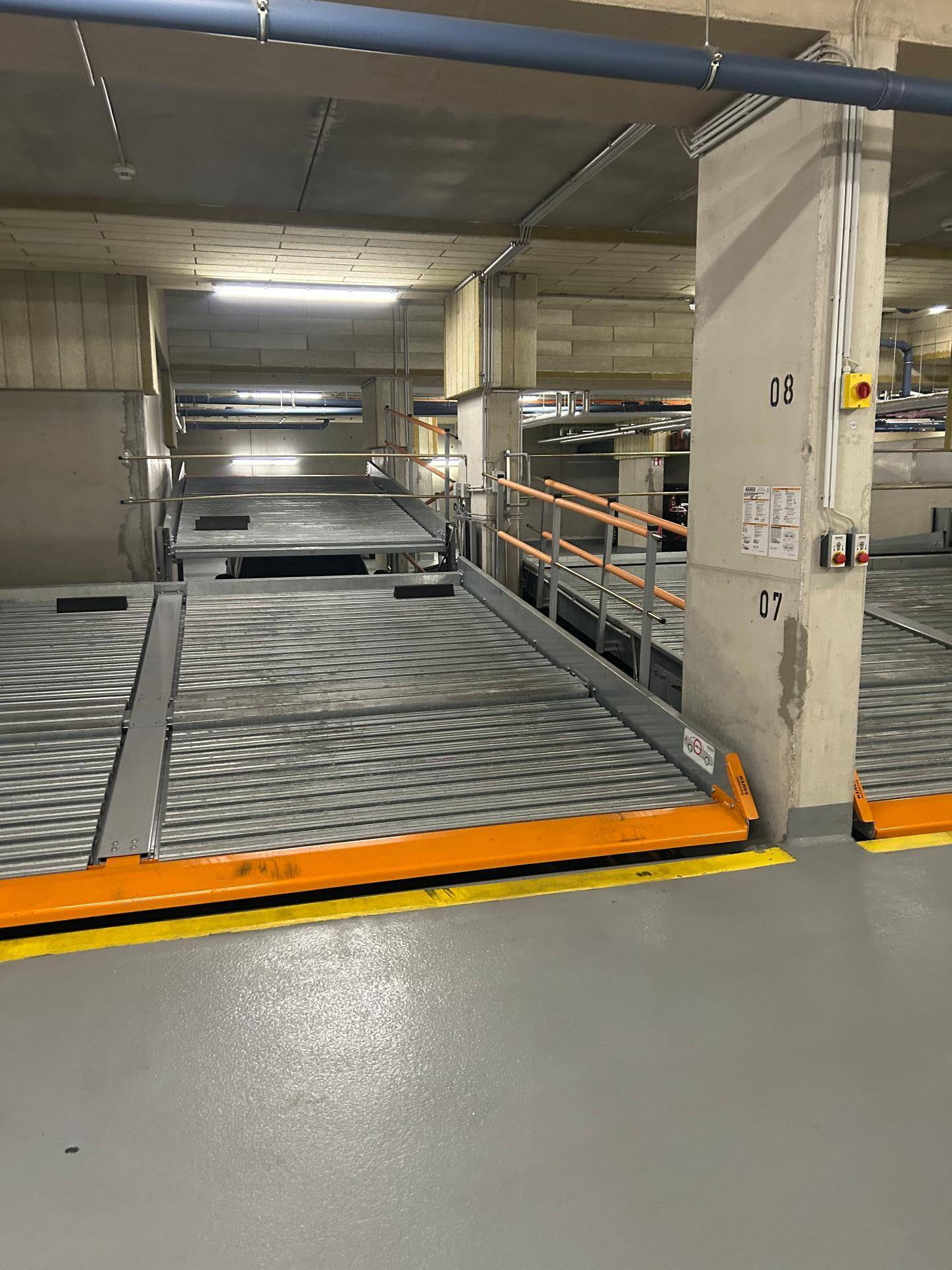 Innenansicht der Tiefgarage mit mechanischen Parkplätzen und robusten Betonsäulen.