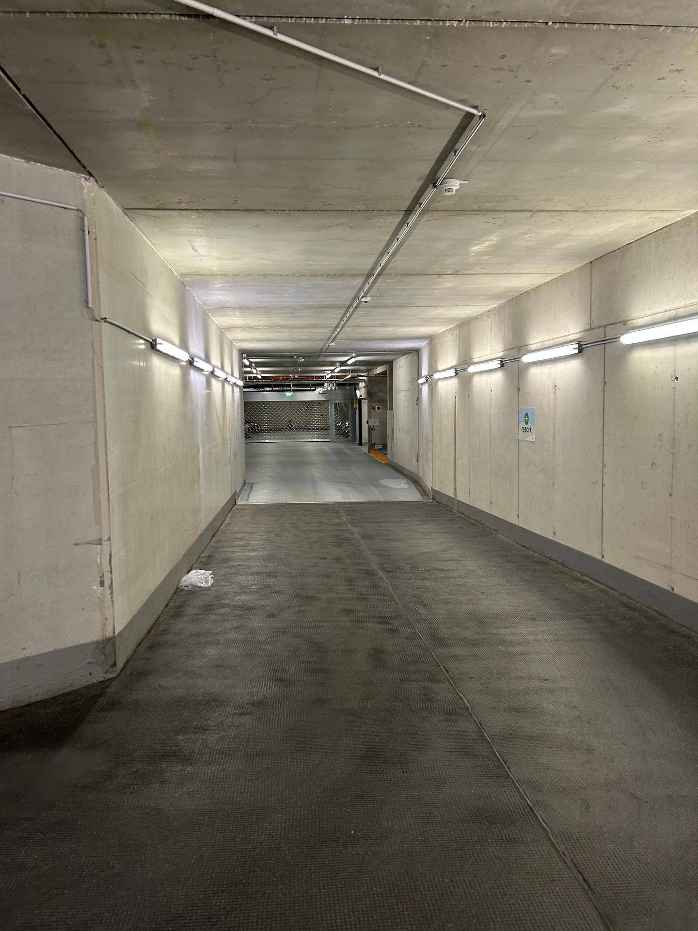 Langer Gang in der Tiefgarage mit durchgehender Beleuchtung und solider Betonstruktur.