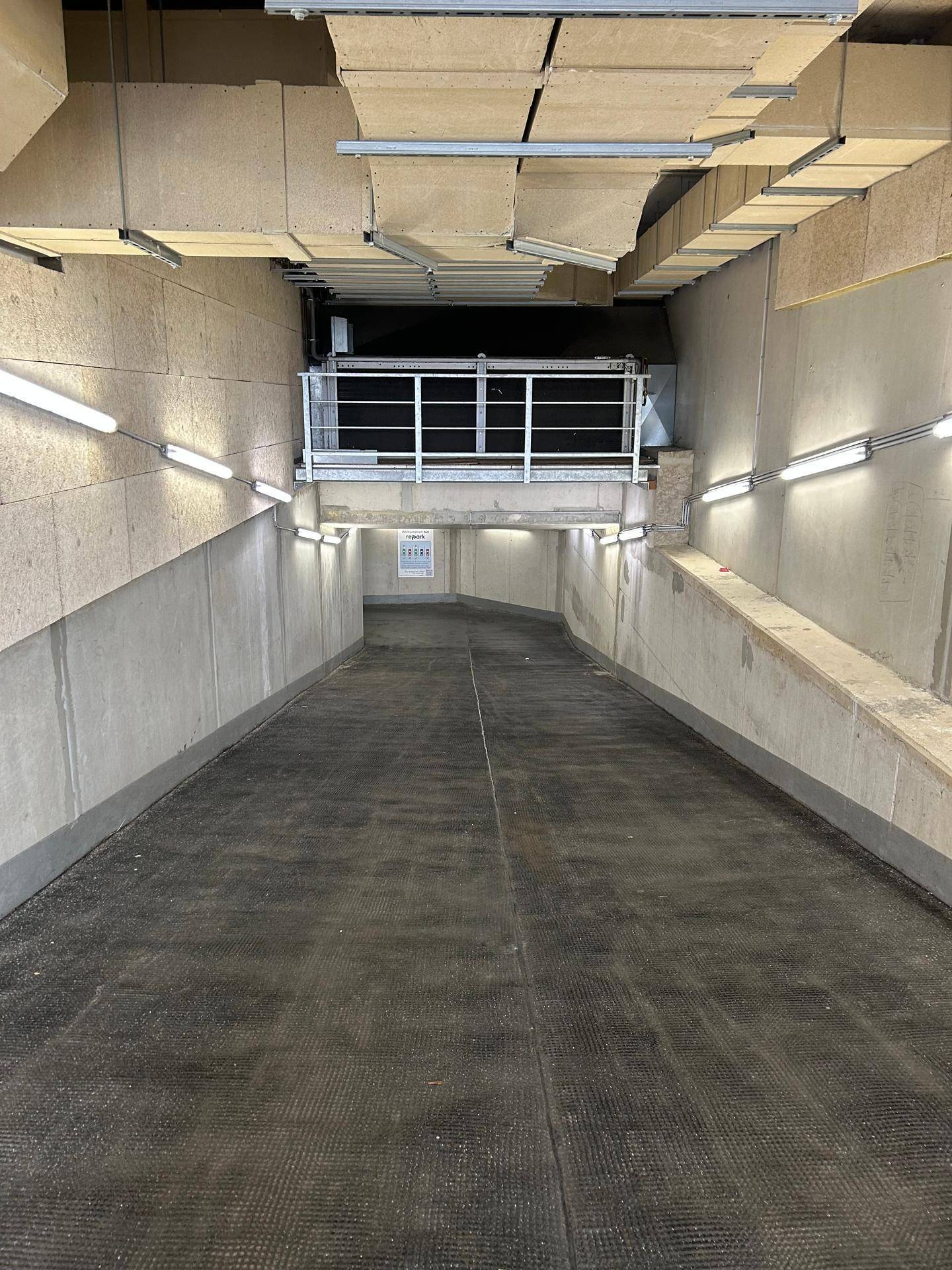 Zufahrtsrampe zur Tiefgarage mit heller Beleuchtung und stabilen Betonwänden.