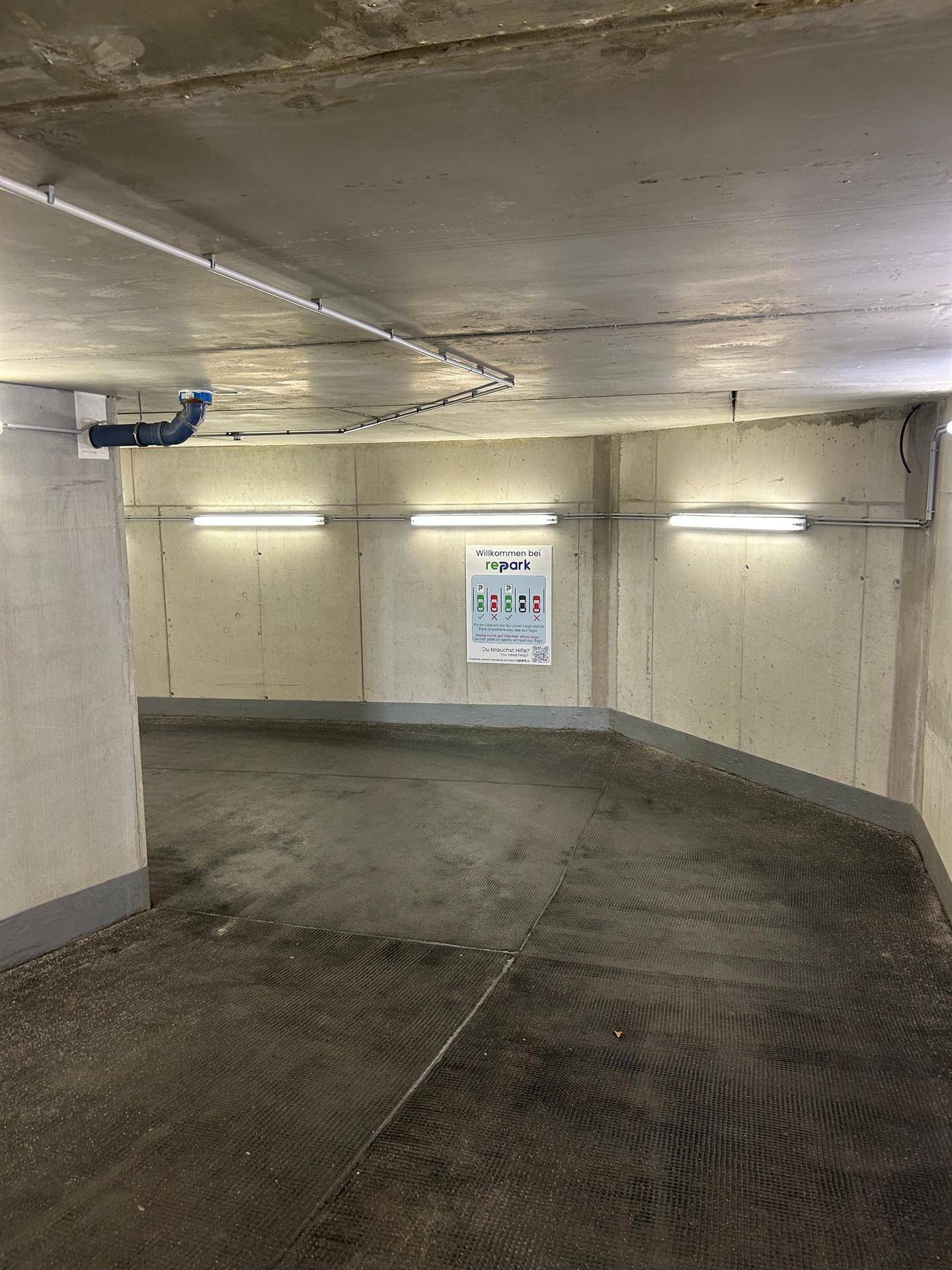 Kurviger Bereich in der Tiefgarage mit Betonwänden und Deckenbeleuchtung, gut ausgeleuchtet.