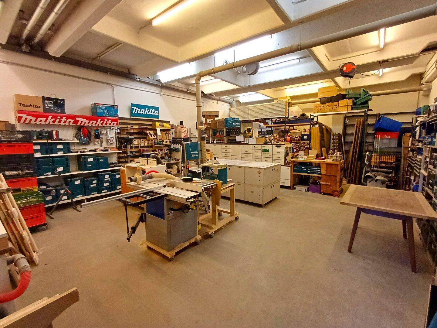Helle Werkstatt mit Holzbearbeitungsmaschinen, Regalen voller Werkzeuge und Arbeitsflächen.