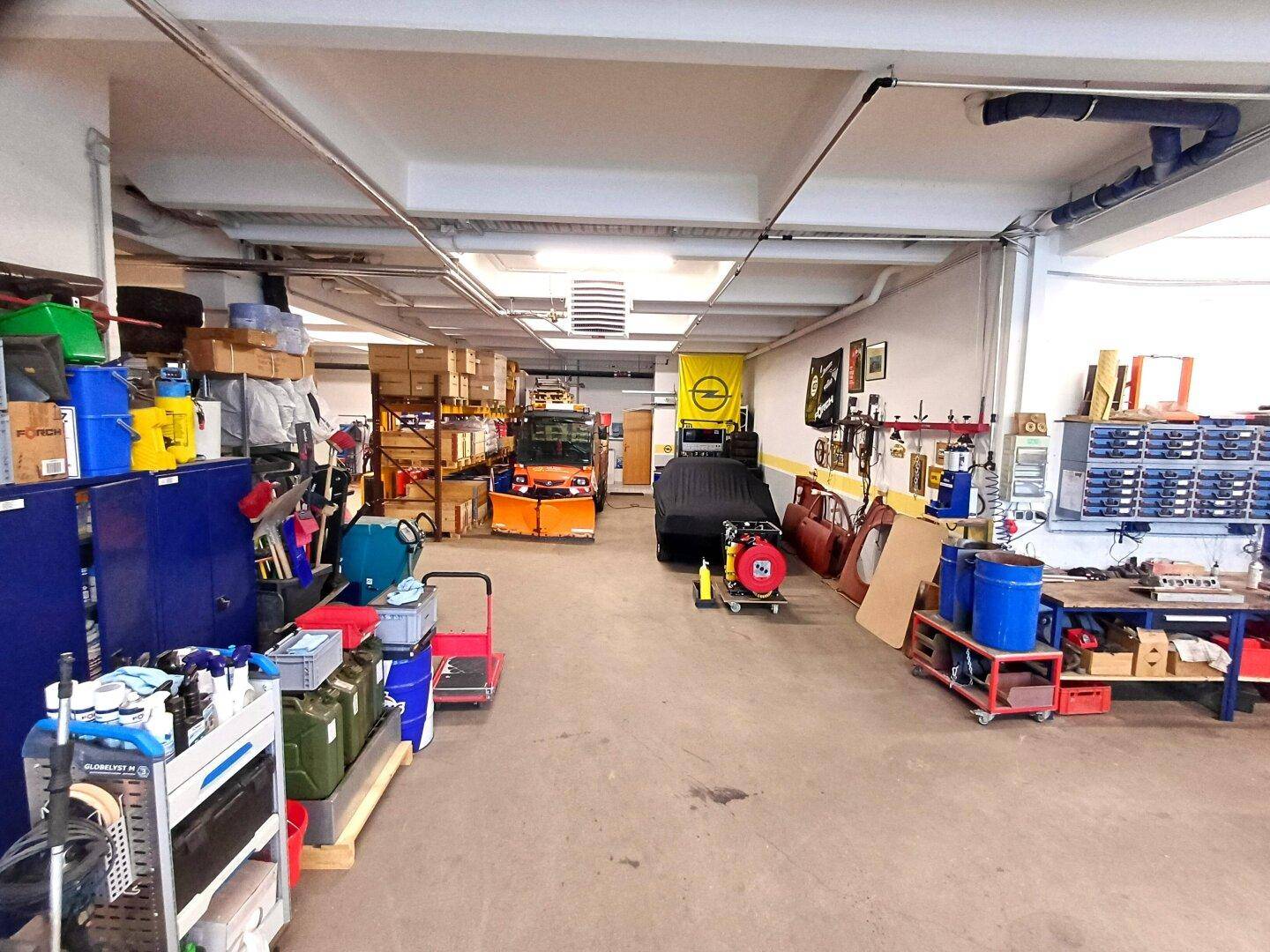 Große Werkstatt mit verschiedenen Arbeitsbereichen, Hebebühne und Lagerregalen für Ersatzteile.
