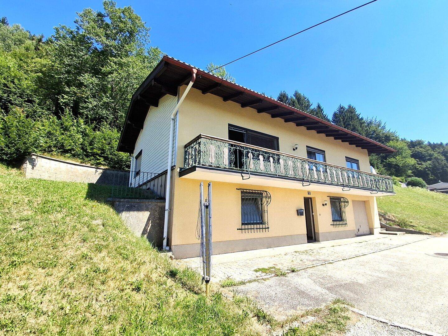 Einfamilienhaus an einem Hang mit Balkon und umgeben von viel Grün.