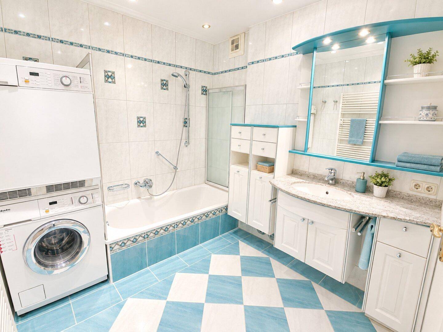 Modernes Badezimmer mit blauen und weißen Fliesen, Badewanne, Dusche und integrierter Waschküche.