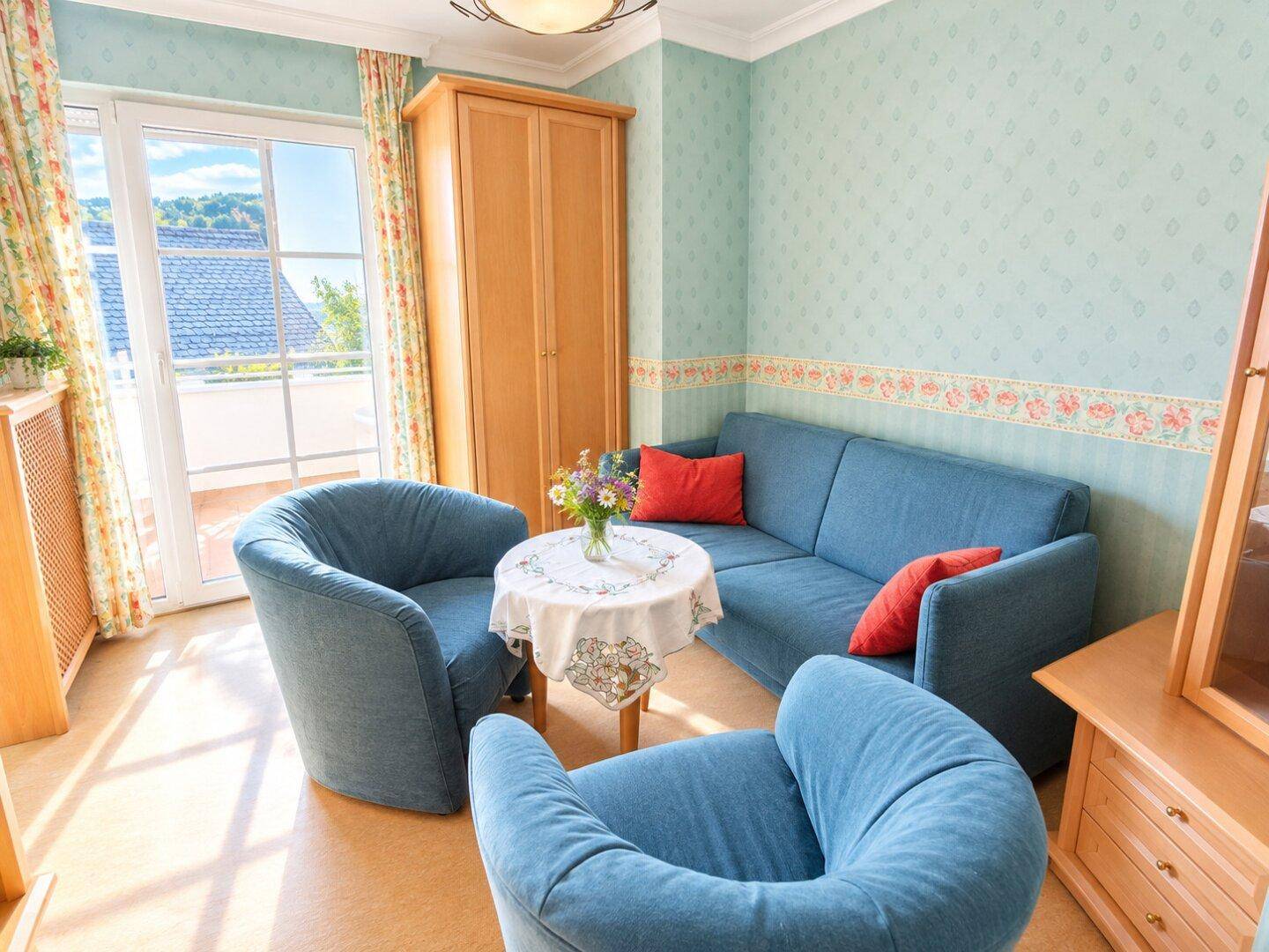 Helles Wohnzimmer mit blauen Sitzmöbeln, gemusterter Tapete und direktem Zugang zum Balkon.