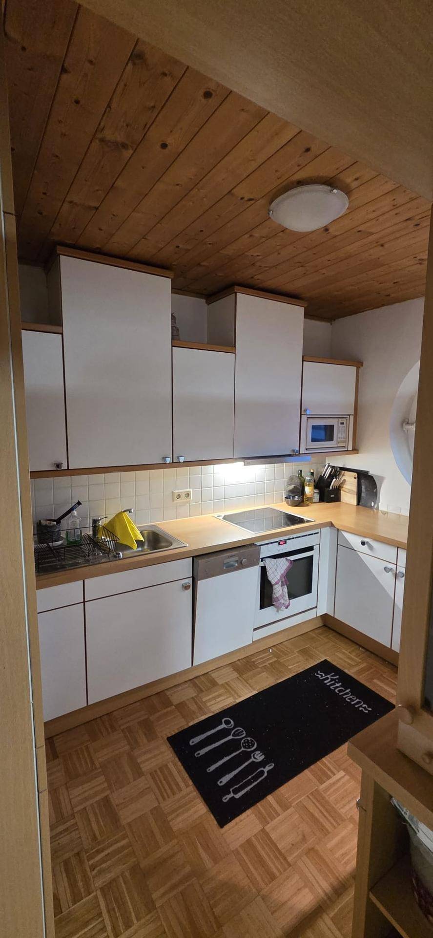 Funktionale Küche mit weißen Schränken, Holzdecke und integrierten Geräten.