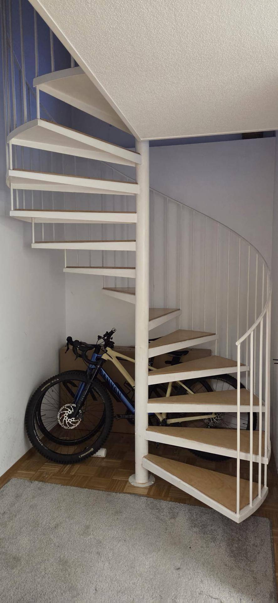 Elegante Wendeltreppe mit Holzstufen und weißem Geländer, die verschiedene Ebenen verbindet.