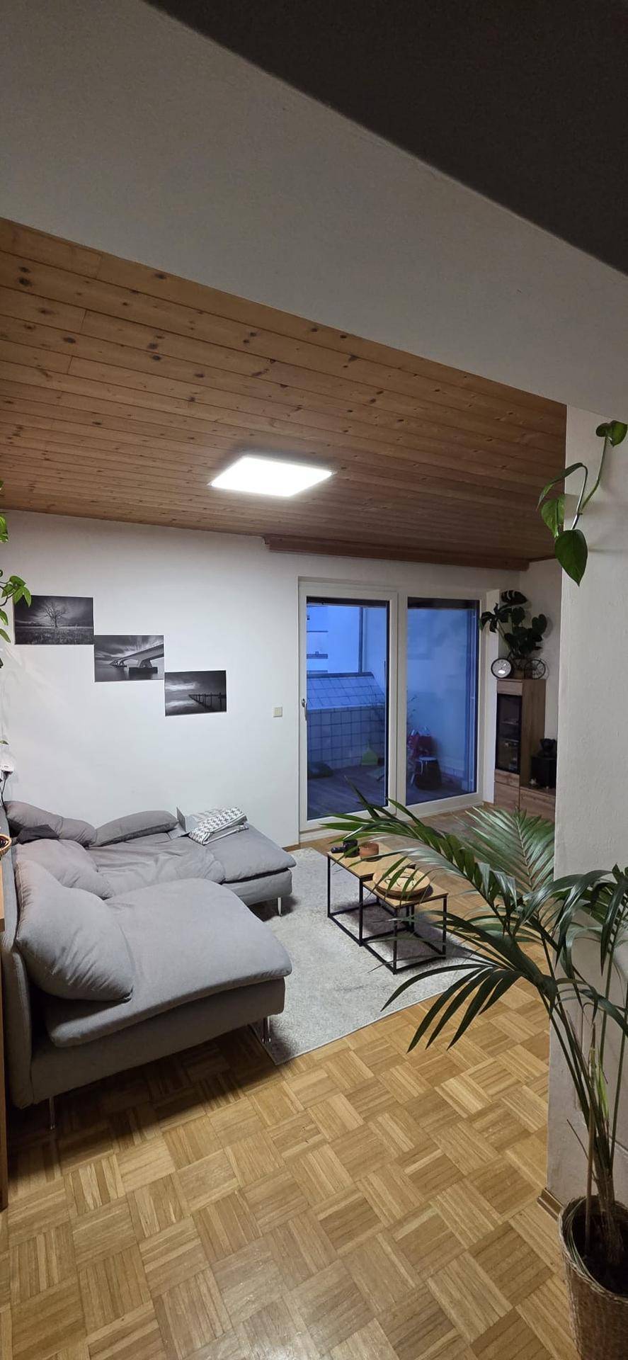 Gemütliches Wohnzimmer mit Holzdecke, Parkettboden und Zugang zur Terrasse.