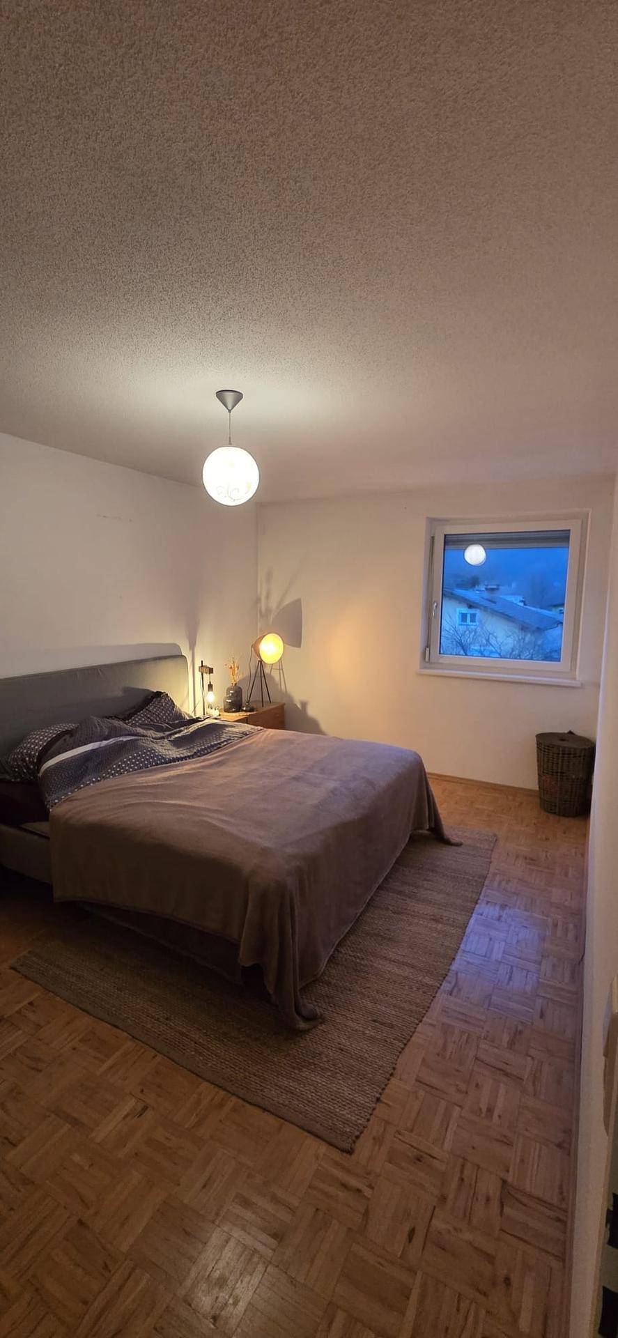 Gemütliches Schlafzimmer mit Parkettboden, großem Bett und Fenster.