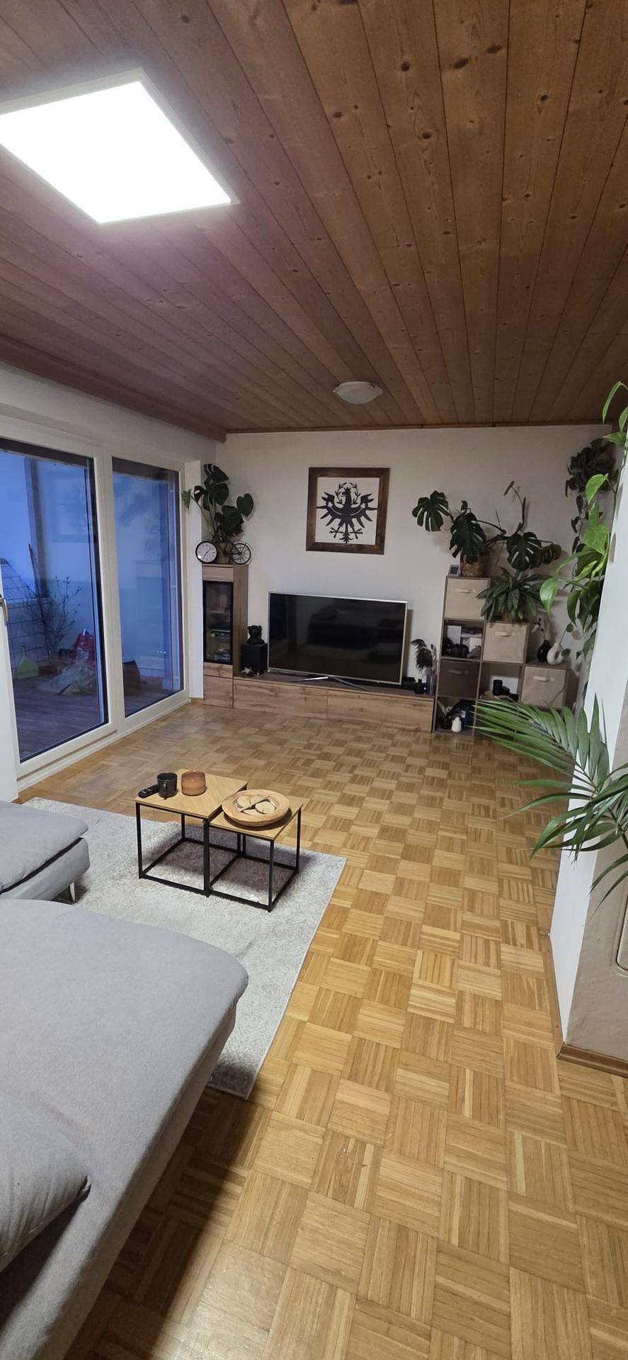 Geräumiges Wohnzimmer mit bequemer Sitzecke, Fernseher und großen Fenstern.