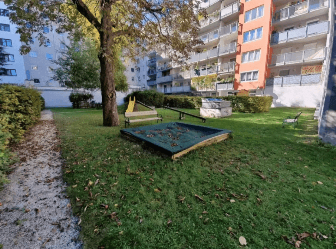 Gemeinschaftlicher Gartenbereich mit Spielplatz, Sandkasten und Sitzbank zwischen Wohngebäuden.
