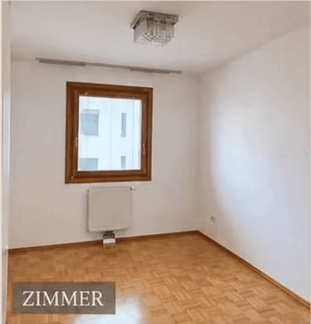 Helles Zimmer mit Parkettboden und einem großen Fenster, ideal als Schlaf- oder Arbeitszimmer.
