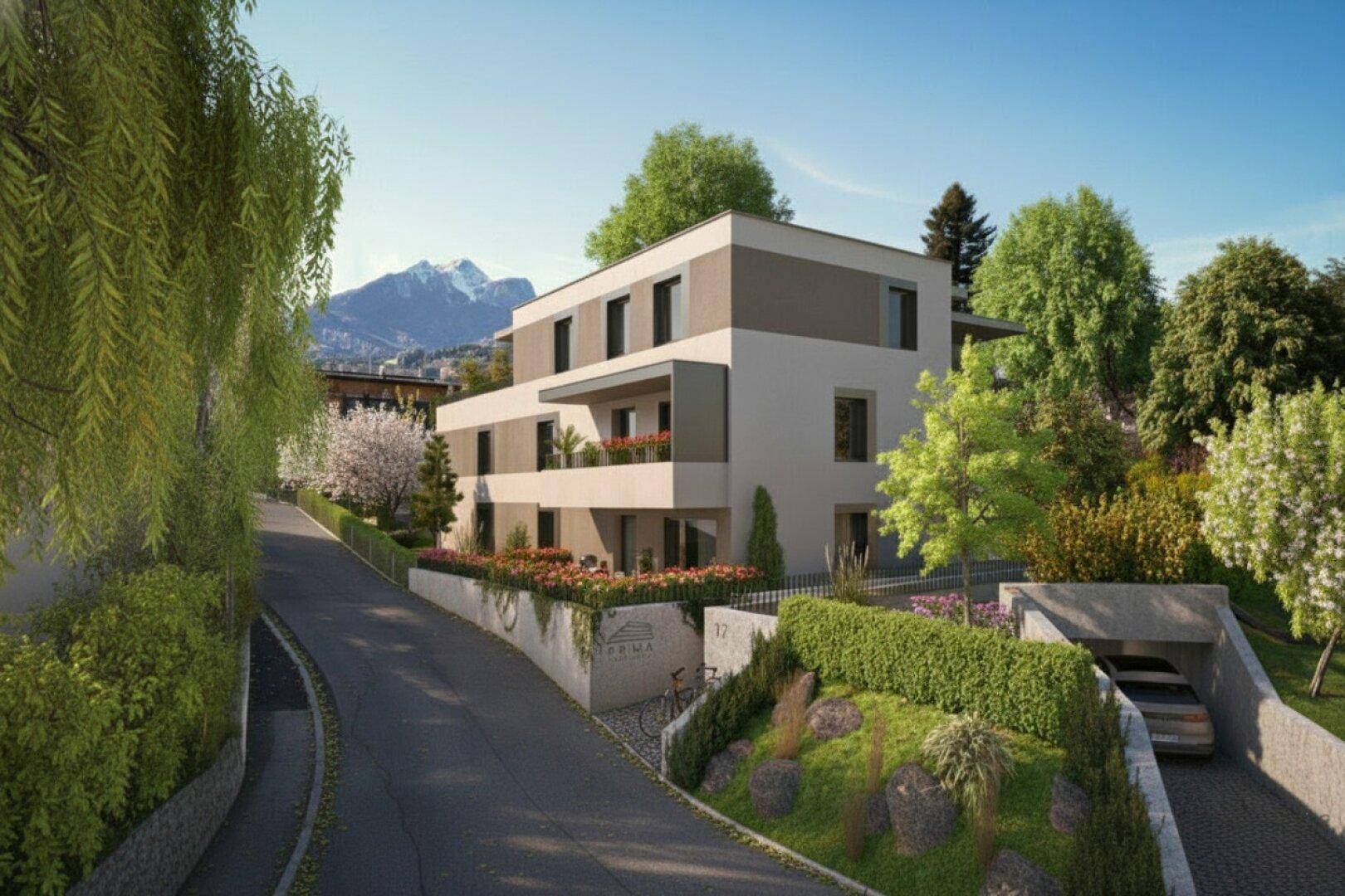 Moderne Wohnanlage mit klarer Architektur, umgeben von viel Grün und Bergblick im Hintergrund.