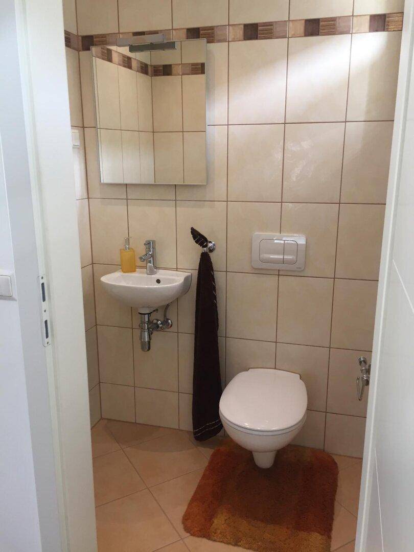 Kleines Gäste-WC mit beigefarbenen Fliesen, Waschbecken und wandhängender Toilette.