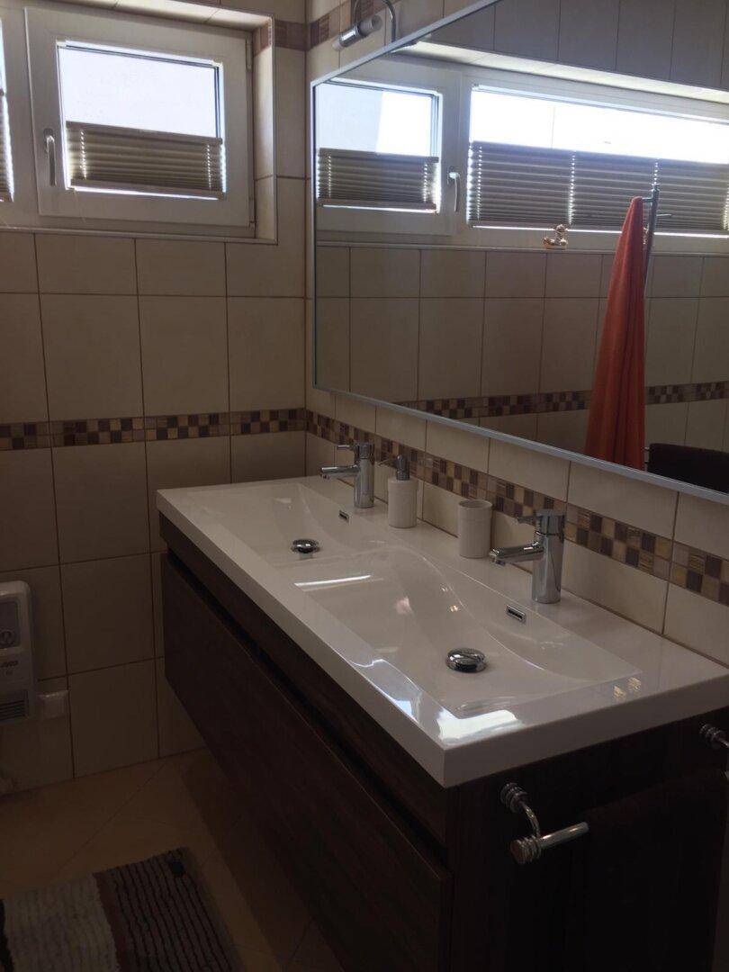 Badezimmer mit Doppelwaschtisch, großem Spiegel und Fenster für natürliches Licht.