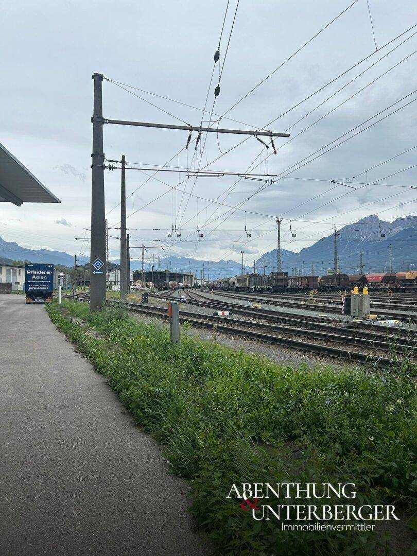 Blick auf Bahngleise und die umliegende Berglandschaft mit etwas Grün im Vordergrund.