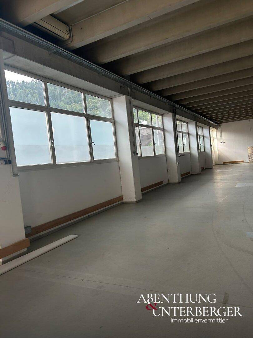 Langer Blick in die Industriehalle mit einer Fensterreihe entlang der Wand und Betondeckenbalken.
