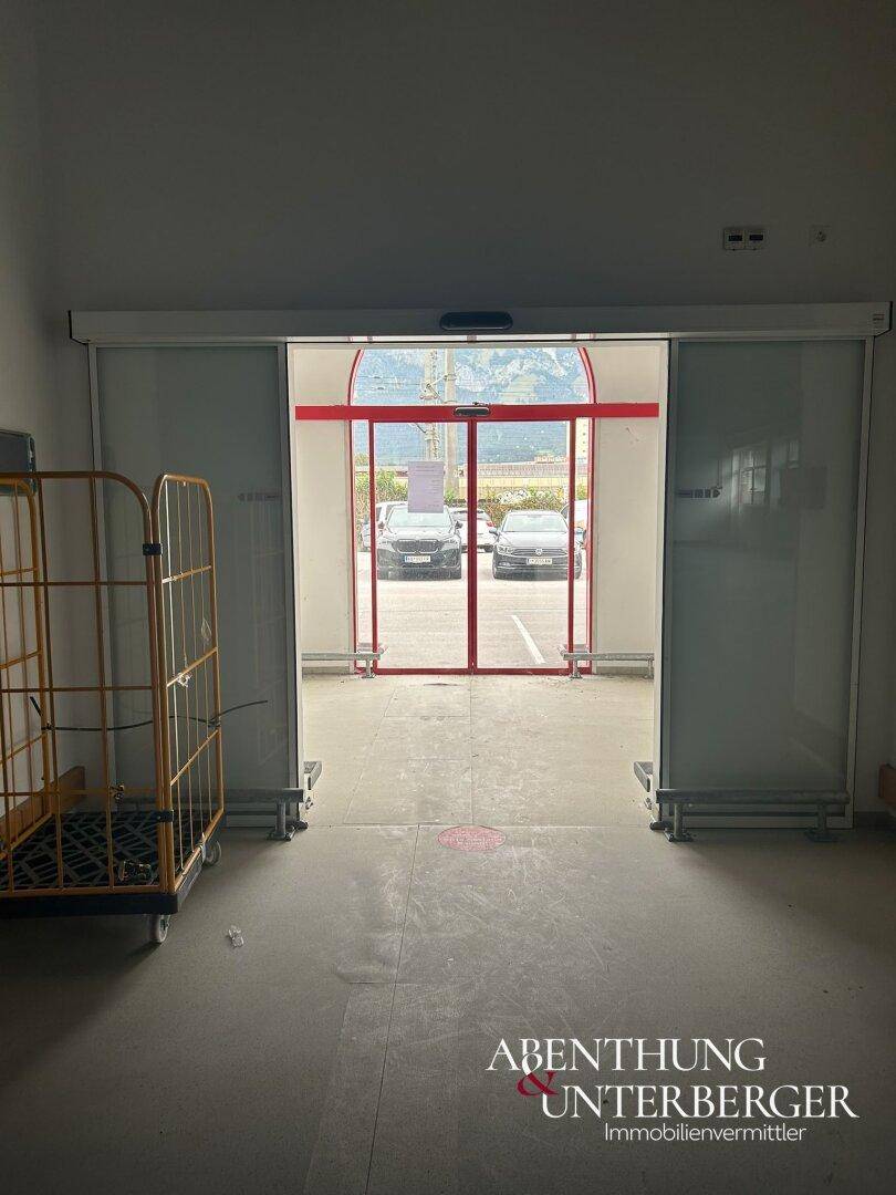 Innenansicht des Eingangsbereichs mit Glasschiebetüren, die den Blick auf den Parkplatz freigeben.