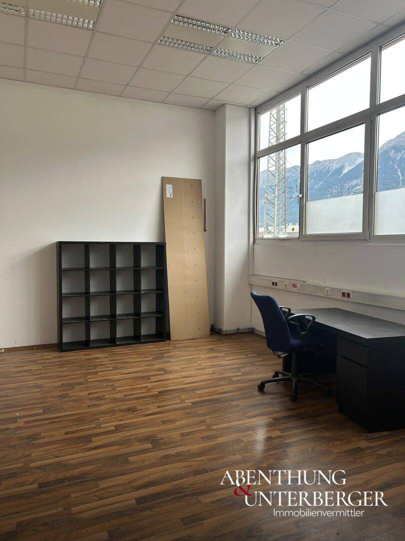 Büroraum mit Laminatboden, großem Fenster mit Bergblick, Schreibtisch und Regal.