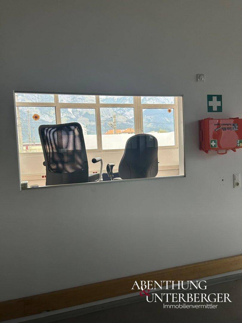 Blick durch ein Innenfenster auf zwei Bürostühle und die Berglandschaft, mit Erste-Hilfe-Kasten an der Wand.