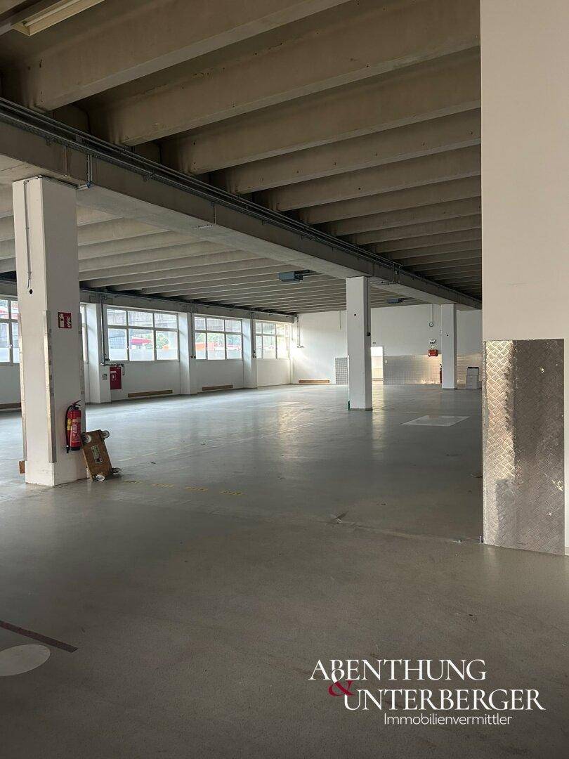 Weitwinkelaufnahme der Industriehalle mit Betonboden, Säulen, Fenstern und einem Feuerlöscher.
