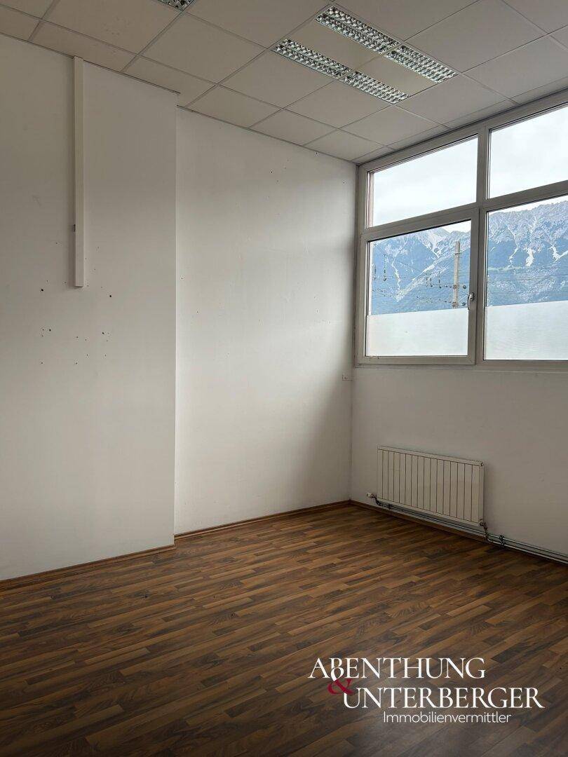 Büroraum mit Laminatboden, Heizkörper und großem Fenster mit Blick auf die Berge.