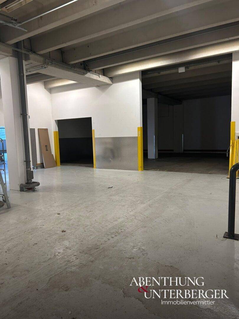 Industriehalle mit breiter Öffnung zu einem weiteren Bereich, gesichert durch gelbe Schutzbarrieren.