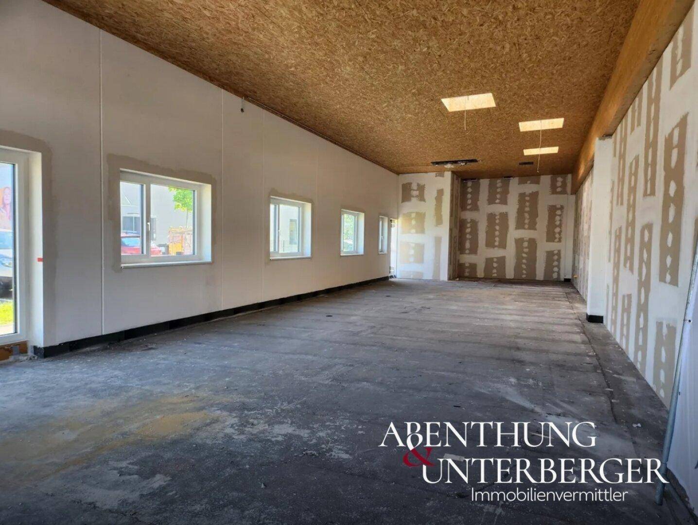 Großer, leerer Gewerberaum im Rohbau mit OSB-Decke, unfertigen Wänden und Betonboden, bereit für den Ausbau.