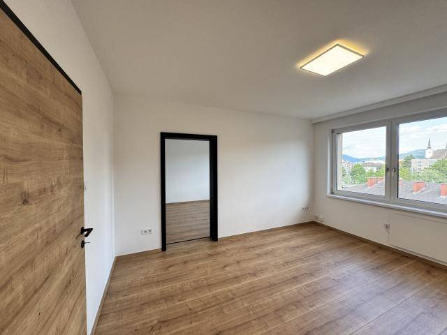 Geräumiges Zimmer mit Laminatboden und weiß gestrichenen Wänden, bietet einen Blick auf die Stadt und Berge.