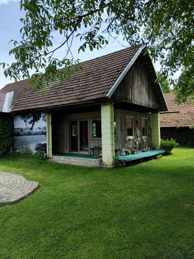 Kleines Holzhaus mit Veranda und einem grünen Rasen unter schattenspendenden Bäumen.